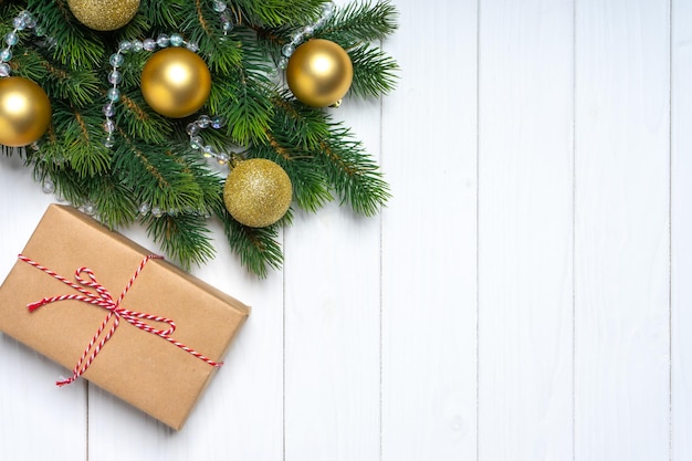 Branche d'arbre de Noël décorée de boules dorées et boîte-cadeau sur fond de bois blanc