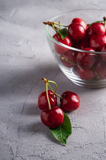 Branche de cerise mûre fraîche près de cerises avec des feuilles vertes dans un bol en verre