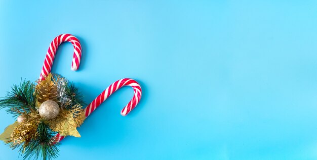 Branche d'épinette avec décorations de Noël et bâtons de caramel sur fond bleu, bannière, carte postale, espace de copie.