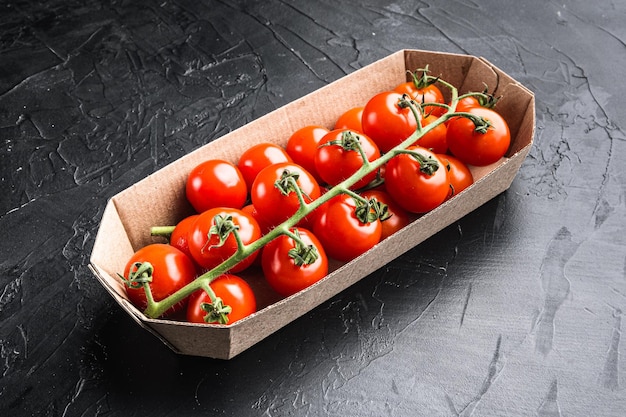 Branche mûre de tomates cerises, dans un récipient, sur fond noir en pierre