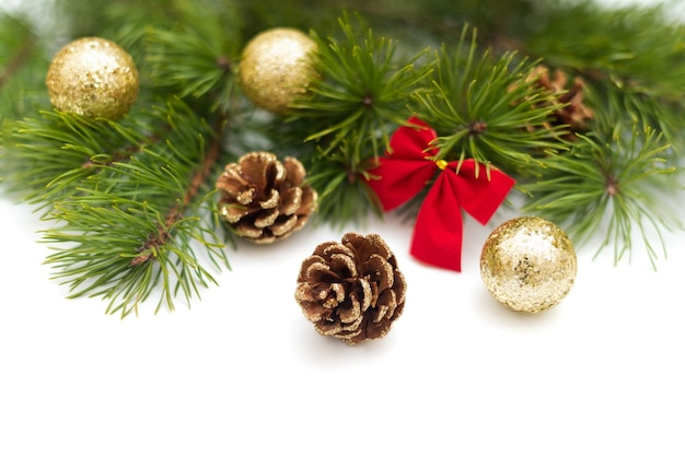 Branche de pin, décorée de pommes de pin à paillettes dorées, de boules dorées brillantes et d'un petit nœud rouge sur fond blanc. Composition de Noël, espace de copie, modèle pour une carte de voeux ou une invitation.