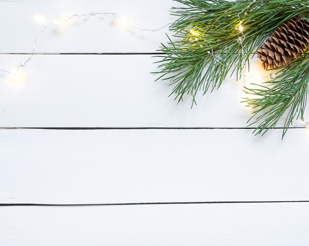 Branche de pin de Noël sur fond en bois blanc avec cônes et guirlande.