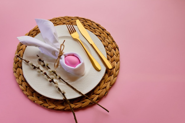 Branche de saule en fleurs, oeuf de pâques sur assiette et vaisselle sur fond rose