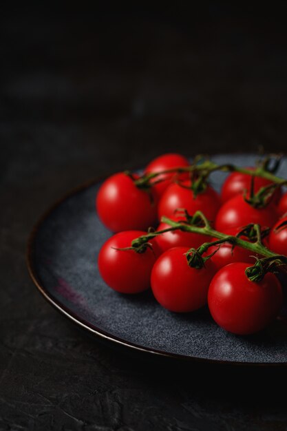 Branche de tomate cerise, légumes biologiques mûrs frais en plaque grise sur une surface noire foncée, angle de vue