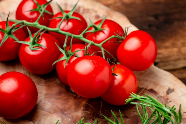 Branche de tomates cerises fraîches avec des verts sur un fond en bois marron