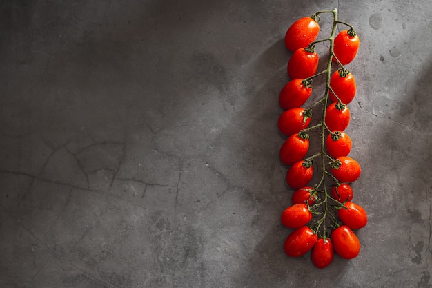 Photo branche de tomates cerises mûres rouges sur fond de pierre grise. mise en page créative