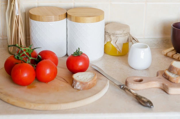 Branche de tomates fraîches mûres et tomates tranchées sur planche à découper en bois. Ingrédient pour la cuisson. Ustensiles de cuisine de style scandinave. Mise au point sélective