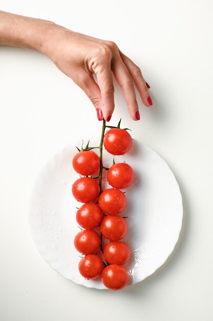 Une branche de tomates à la main sur une plaque blanche