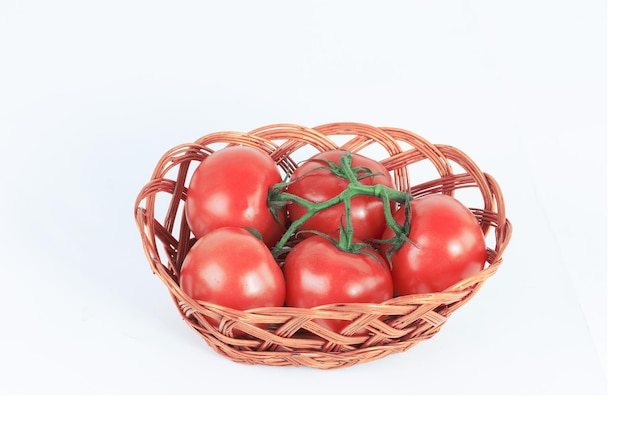 Branche de tomates mûres dans un panier en osier isolé sur blanc