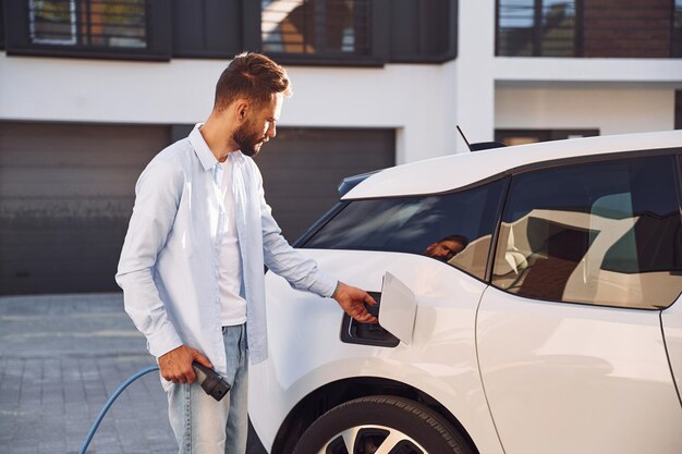 Brancher le câble de charge Jeune homme élégant est avec une voiture électrique pendant la journée