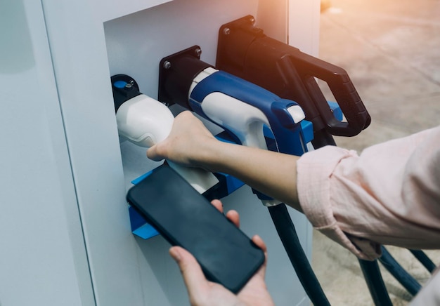 Brancher à la main un chargeur dans une prise de voiture électriqueLa voiture électrique ou le véhicule électrique se recharge à la station