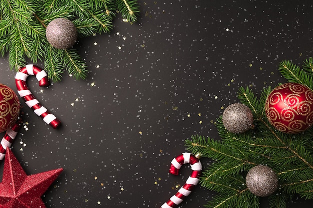 Branches d'arbres de Noël avec des boules rouges et or et canne en bonbon sur fond noir avec de la neige en vue de dessus