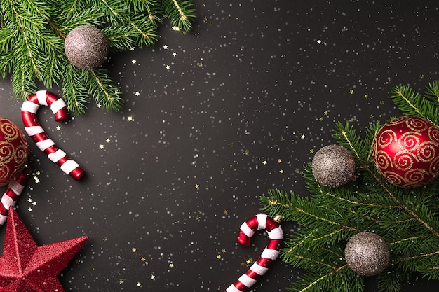 Photo branches d'arbres de noël avec des boules rouges et or et canne en bonbon sur fond noir avec de la neige en vue de dessus