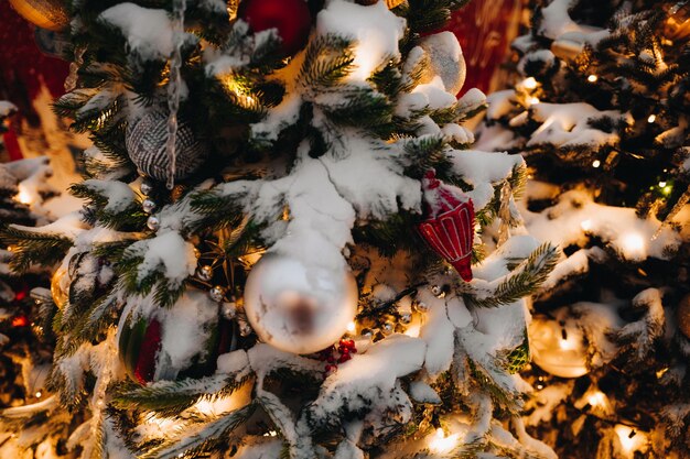 Branches d'arbres de Noël couvertes de neige décorées de boules de fête dorées, jouets et lumières Nouvel an