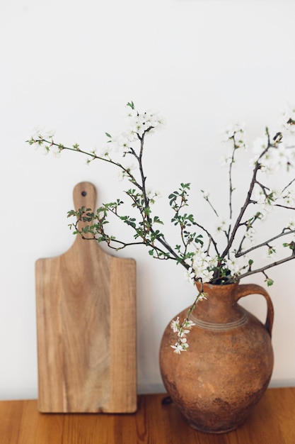 Branches de cerisier en fleurs dans un vieux vase et planche de bois sur une table contre un mur blanc Fleurs de printemps dans la cuisine nature morte Campagne simple vivant à la maison décor rustique Bonjour printemps