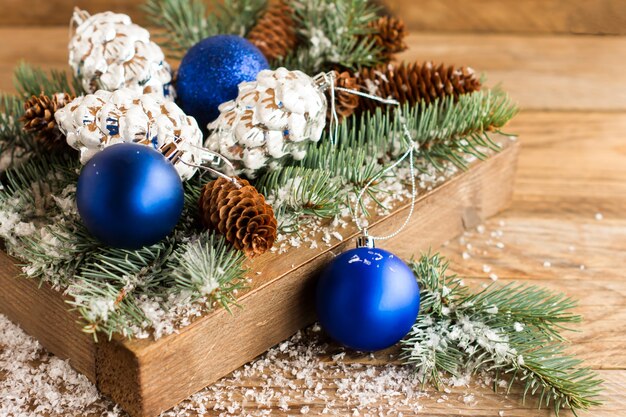 Des branches couvertes de neige ont mangé avec des cônes et des jouets de Noël dans une boîte en bois sur la table du village.