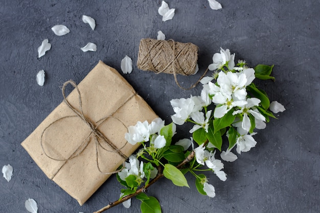 Branches fleuries de cerisier, pommier sur fond gris. Composition florale. Jolie boîte cadeau enveloppée de papier kraft brun et décorée de jute, vue de dessus, avec un espace pour le texte