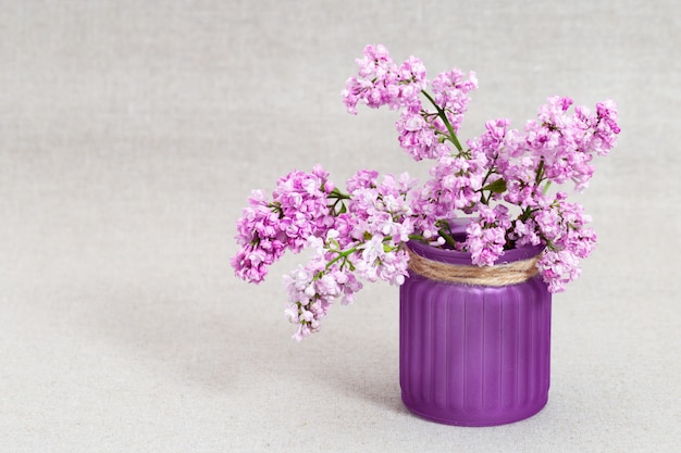 Branches de lilas rose en fleurs dans un vase sur fond de tissu flou avec espace de copie.