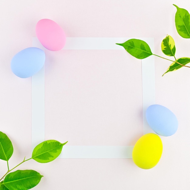 Branches d'oeufs de pâques avec des feuilles vertes et un cadre blanc sur fond rose