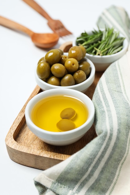Des branches d'olive, de l'huile et des olives dans des bols, une serviette sur fond blanc, vue de haut