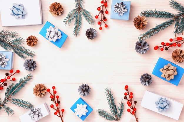 Les branches de sapin, les fruits rouges, les petites boîtes et les cônes se trouvent en cercle. Cadeaux décorés d'arcs en argent et en or. Sur un espace de copie de fond en bois clair.