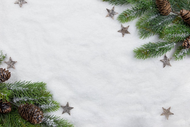 Branches de sapin de Noël à plat avec pommes de pin et décoration sur fond de neige. Composition créative avec bordure. Vue de dessus. Espace de copie.