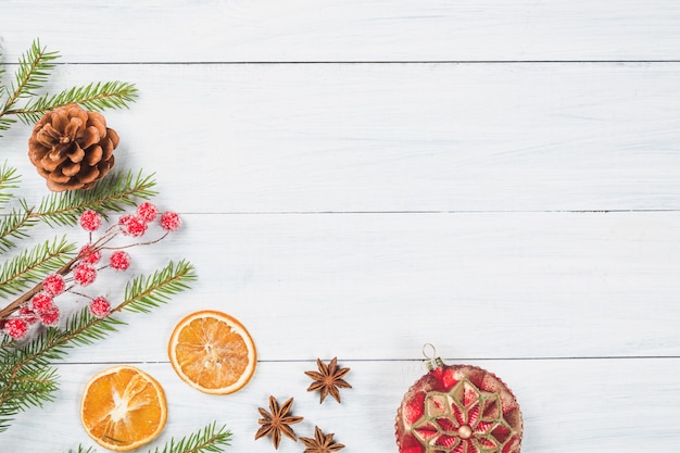 Branches de sapin avec orange séchée, étoiles d'anis, boule de Noël et cône sur un fond en bois blanc.