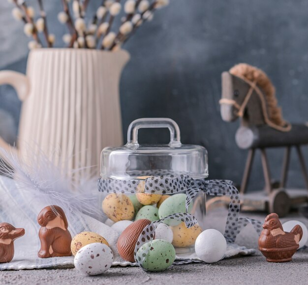 Branches de saule dans un vase sur fond gris et oeufs en chocolat colorés pour les vacances de Pâques.