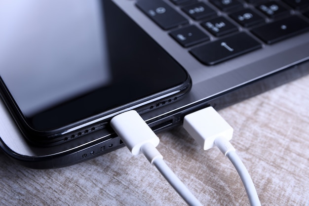 Branchez le cordon USB, le chargeur de câble, la charge, la charge et le transfert de données du mobile un téléphone, un smartphone avec un ordinateur portable sur un plancher en bois, une table Vue de dessus