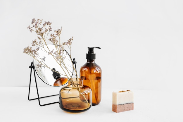 Branchez des fleurs dans un vase en verre, un miroir, des bouteilles de shampoing et du savon sur une table blanche. Décor pour l'intérieur. Décoration élégante pour la maison.