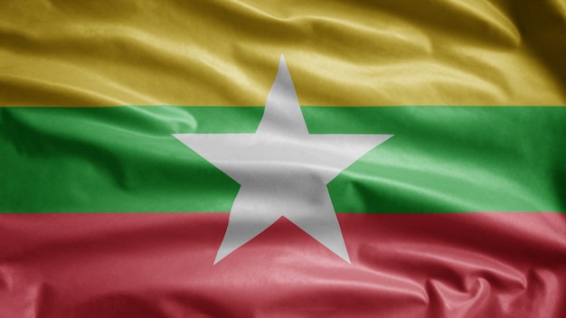 Brandir le drapeau du Myanmar sur le vent. Gros plan de la bannière birmane soufflant de la soie lisse. Enseigne de texture de tissu en tissu