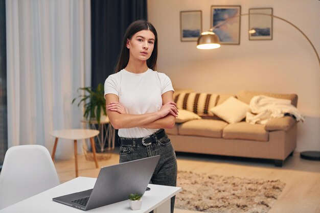 Bras croisés Femme en chemise blanche et jeans noirs se tient à l'intérieur à la maison