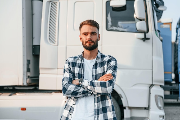 Avec les bras croisés, le jeune chauffeur de camion est avec son véhicule pendant la journée