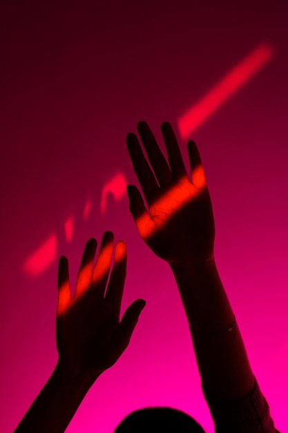 Bras de femme faisant des gestes avec la main ouverte sur la tache rouge néon de fond rose de mode sur le minimalisme de poignet