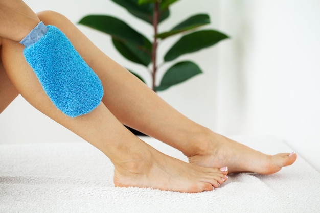 Bras de femme tenant une brosse sèche bleue au sommet de sa jambe traitement de la cellulite et brossage à sec