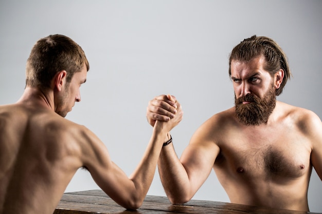 Bras de fer. Homme barbu fortement musclé luttant contre un homme faible et chétif.