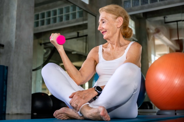 Bras de formation caucasien femme senior avec haltère au gymnase de remise en forme.