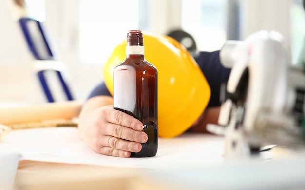 Le bras d'un ouvrier ivre avec un casque jaune tient de l'alcool.