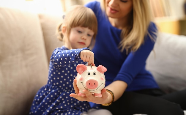 Le bras d'une petite fille mettant des pièces dans la tirelire