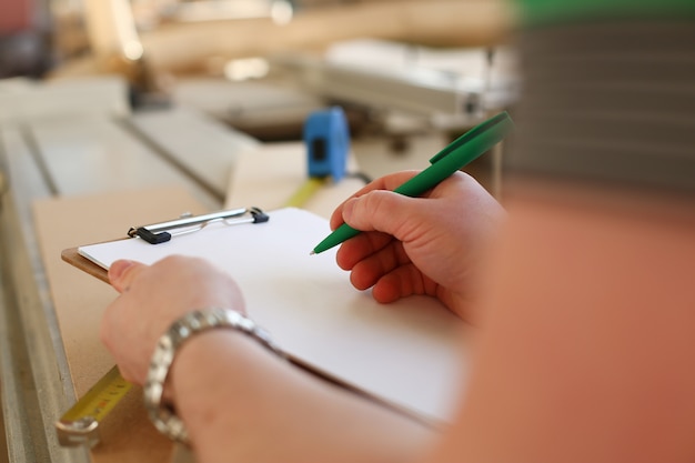 Bras de travailleur prenant des notes sur le presse-papiers avec stylo vert