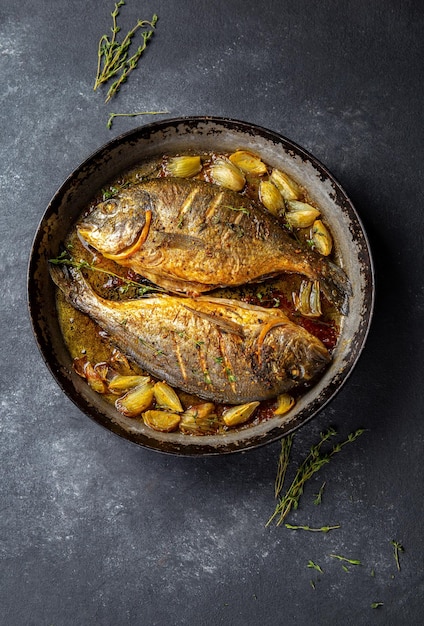 Brasse de mer cuite au four ou dorada avec oignon et herbes dans une casserole sur fond sombre