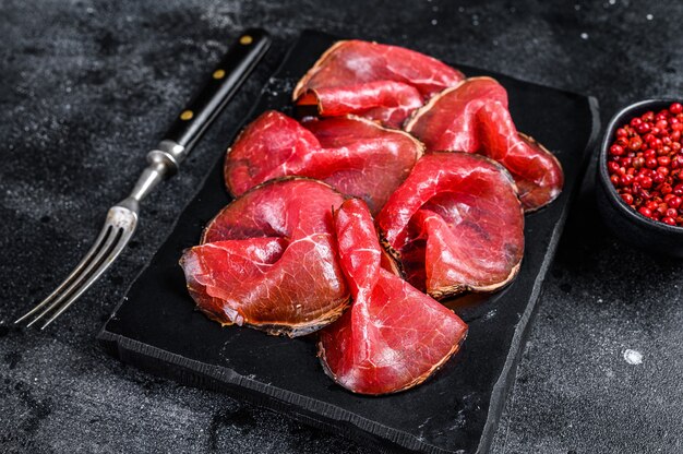 Bresaola, viande séchée, morceaux de bœuf, Antipasti italiens. Fond noir. Vue de dessus.