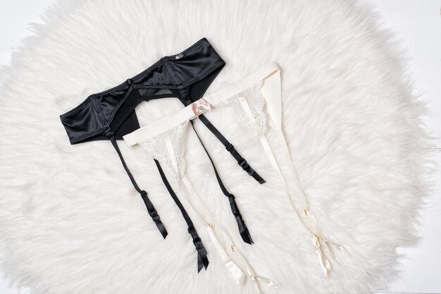 Bretelles noires et blanches pour bas sur fourrure blanche. Fermer. Concept de lingerie mode