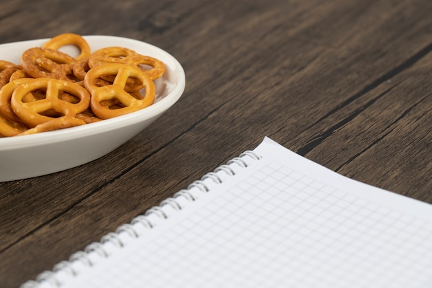 Bretzels craquelins salés avec cahier blanc ouvert placé sur une table en bois.