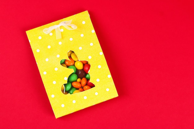 Bricolage de Pâques emballant des bonbons dans un sac avec une silhouette de lapin découpée sur un fond rouge.
