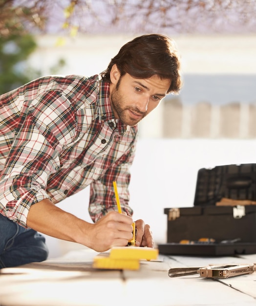 Bricolage qualifié Un beau jeune charpentier prenant des mesures de bois