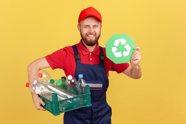 Bricoleur barbu debout et tenant une pancarte de recyclage et une boîte avec des bouteilles en plastique