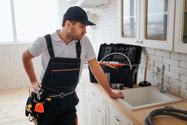 bricoleur occupé se tenir dans la cuisine à l'évier et le regarder