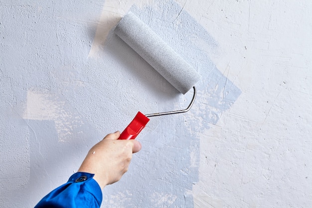 Bricoleur peint le mur à l'aide d'un rouleau à peinture et de peintures lors de la rénovation