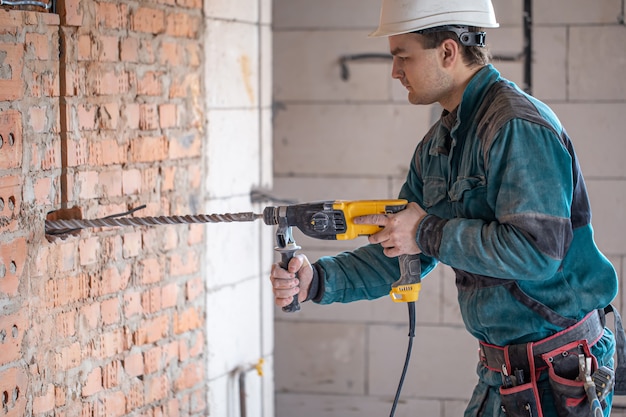 Bricoleur en train de percer un mur avec un perforateur.